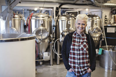 Portrait of smiling female manager standing with hands in pockets at brewery