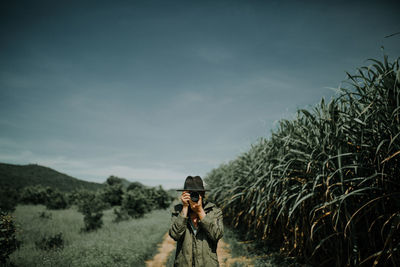 Close-up of person photographing while standing amidst plants against sky