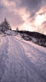 Snow covered landscape against sky during sunset