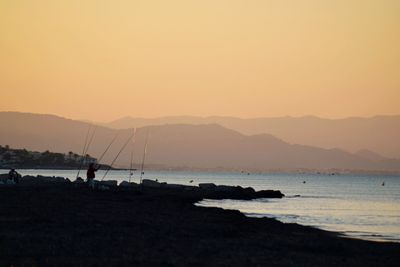 Silhouette people on beach against clear sky during sunset