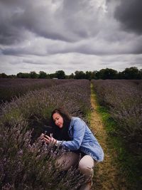 Woman standing by purple flowers on field against cloudy sky