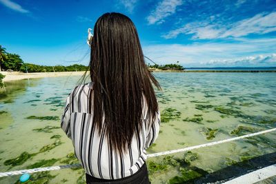 Rear view of woman standing by sea against sky