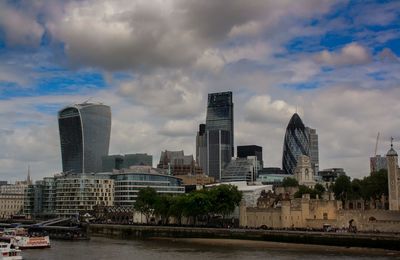 Buildings by river against sky in city