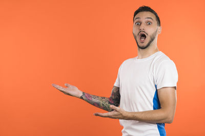 Portrait of young man with arms raised standing against yellow background