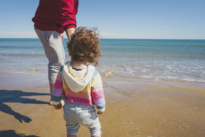 Rear view of boy standing at beach against clear sky