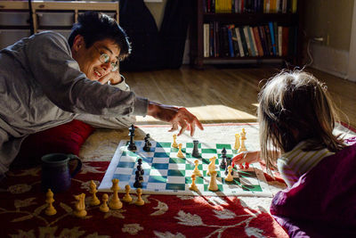 A smiling dad and his young girl play chess in a patch of bright light