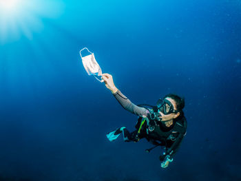 Full length of woman holding surgical mask swimming in sea