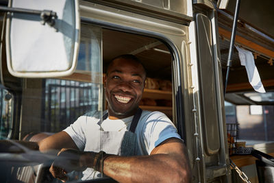 Smiling mid adult salesman looking away while driving food truck in city