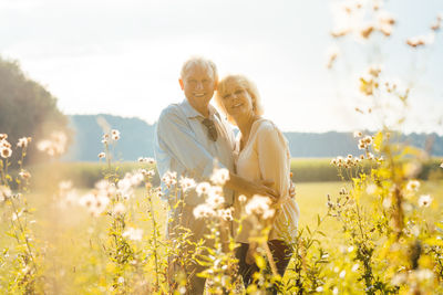 Senior couple on a sunlit meadow embracing each other looking at the camera