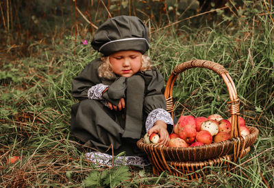 Full length of cute girl with apples in basket on grass