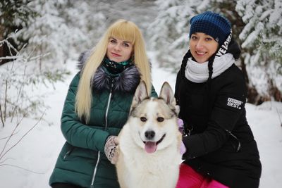 Portrait of smiling young woman with dog standing in snow