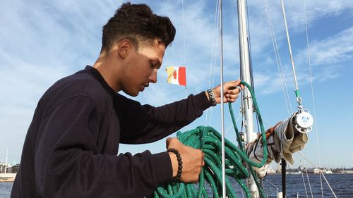 Side view of young man holding sailboat in sea against sky