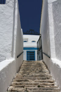 Low angle view of steps between white walls leading towards building to a clear blue sky
