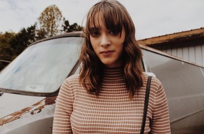 Portrait of girl standing by car against sky