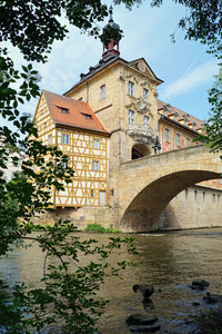 Arch bridge over river by building against sky