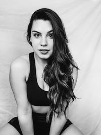 Portrait of beautiful woman sitting against curtain