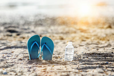 Flip flops on beach sand with water in bottle and sunbeam