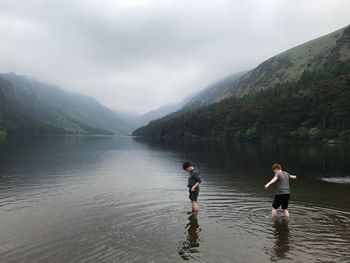 Boys walking in lake against sky