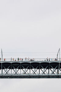 People on bridge over sea against clear sky