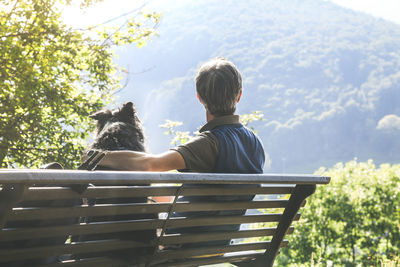 Man and his dog sitting on a park bench looking the mountain panorama. friends together at the park
