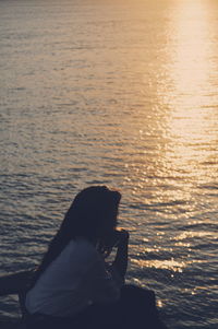 Young woman sitting on lake against sky during sunset