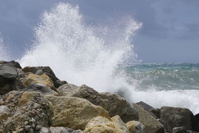 Waves splashing on rocks at shore against sky