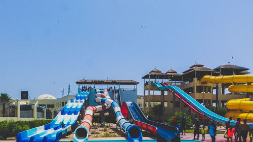 Low angle view of people on playground against clear blue sky