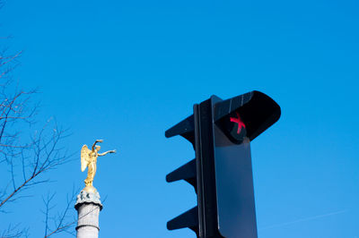 Low angle view of road signal and sculpture against clear blue sky