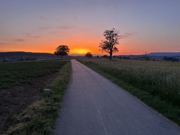 Road amidst field against sky during sunset