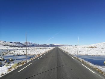 Road amidst snow covered mountains against clear blue sky