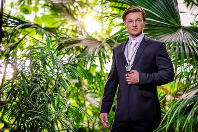Handsome bridegroom wearing suit while standing amidst plants at botanical garden