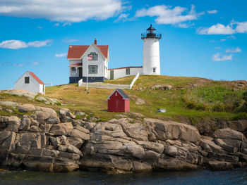 Lighthouse on rock by building against sky