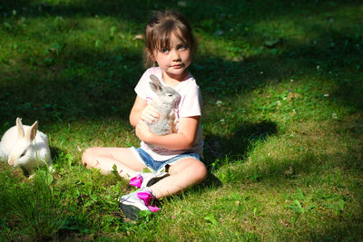 Full length of girl with rabbit sitting on field