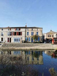 Buildings by river against clear blue sky