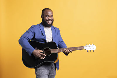 Portrait of man playing guitar against yellow background