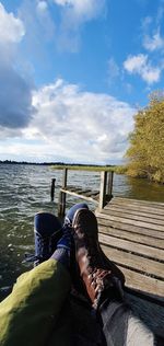 Low section of man sitting on shore against sky