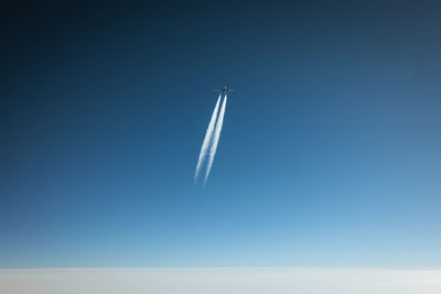 Low angle view of airplane flying against clear blue sky