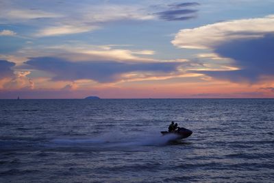 People jet boating in sea against sky during sunset