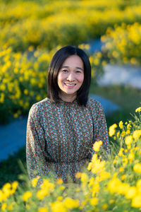 Portrait of smiling young woman with yellow flower in field