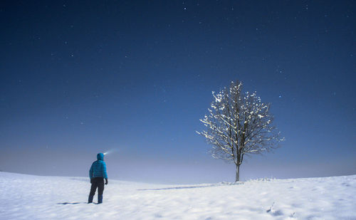 Rear view of man standing on snow against sky at night