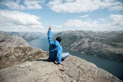 Rear view of man sitting on rock against sky