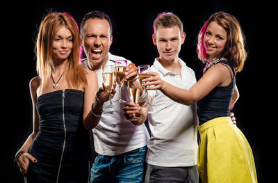 Friends holding champagne flutes while standing against black background