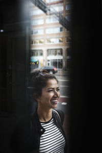 Smiling woman standing in city seen through window