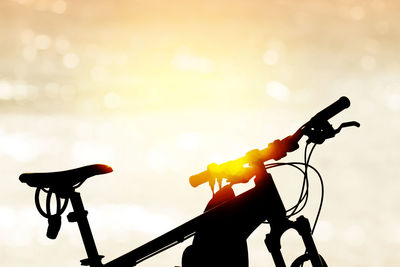 Close-up of silhouette bicycle on illuminated street against sky during sunset