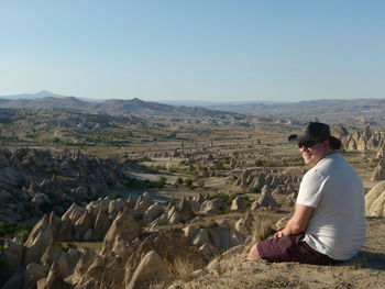 Smiling man sitting on landscape against clear sky