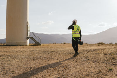 Technician with toolbox walking towards wind turbine