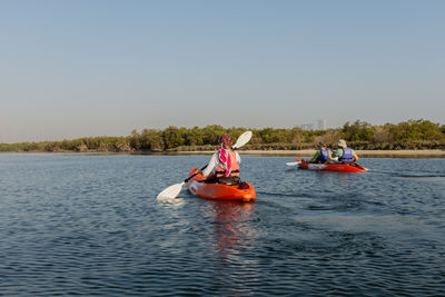 People rowing boat in lake against clear sky