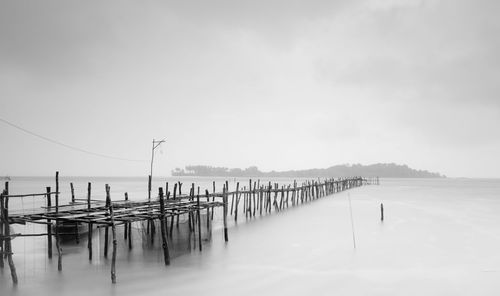 Wooden posts in sea against sky during winter