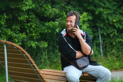 Happy man talking on phone while sitting on bench at park