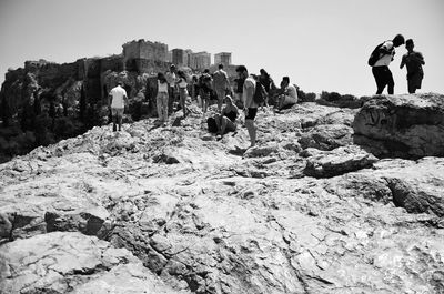 People standing on rock by sea against clear sky